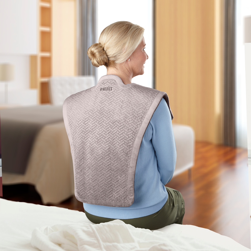 Una persona usando la envoltura de masaje con vibración y calor de Homedics sobre sus hombros.