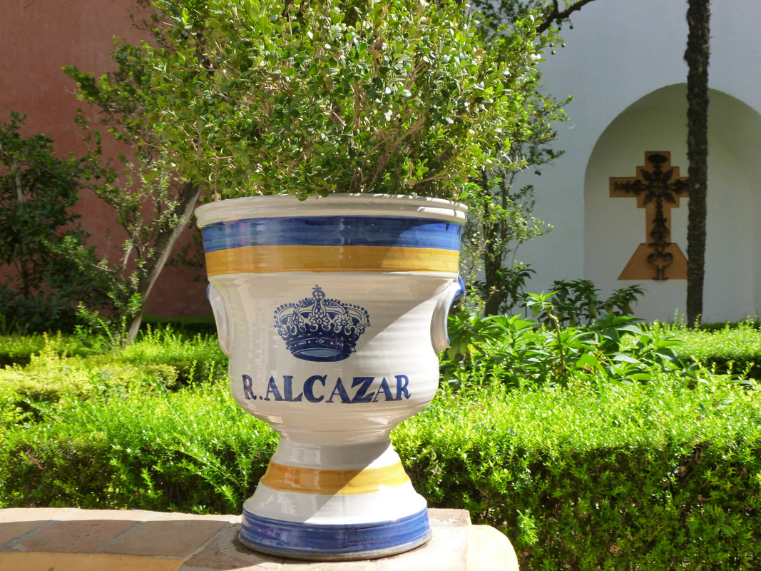 A pottery plant pot, white, with golden yellow and mid blue hoops. It has R. Alcazar and a crown painted on it.