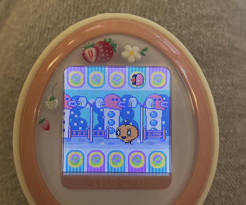 close up photograph of a tamagotchi plus color device. memetchi is walking with determination to the matchmaking/dating building