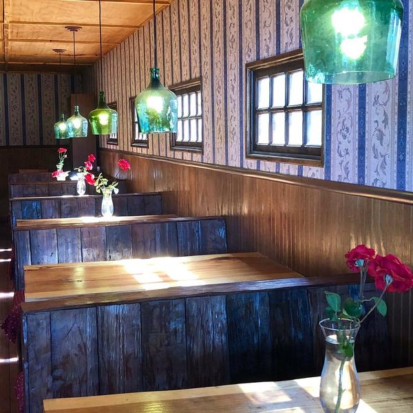 Comedor con bancas de madera, lámparas de vidrio verde y rosas en las mesas de Cervecería Rural