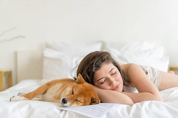 Woman and Shiba Inu sleeping on bed with papers.