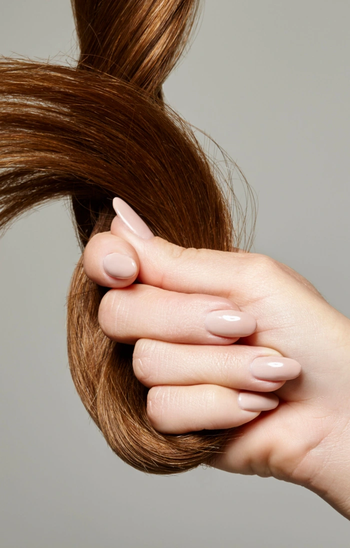 A woman's hand with beautiful nails holds brown hair