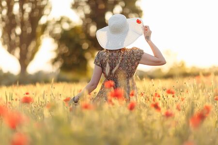 141410340-redhead-woman-in-hat-on-green-field-with-poppies-in-summer-sunset.jpg