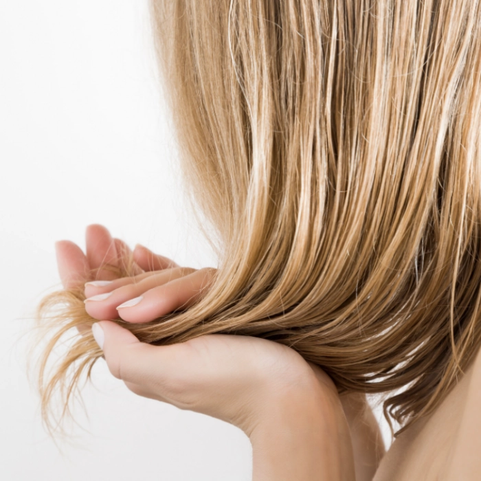 A blonde with hair loss holds her hair in her hands