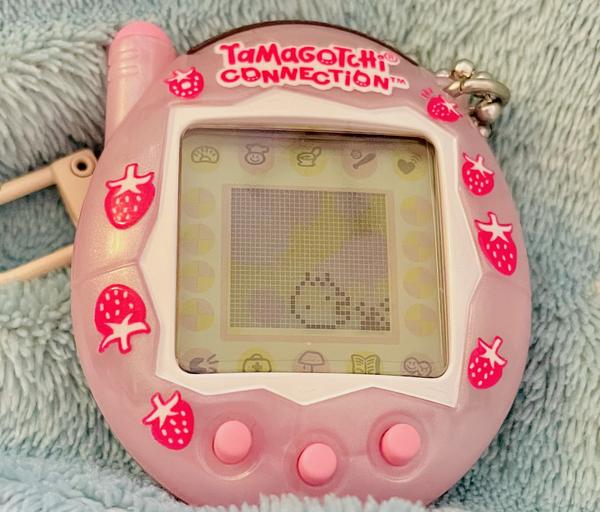 up close photo of a tamagotchi connection device (2024 rerelease) showing ALIBI standing next to her own feces, facing it with her mouth open and smiling wide like she might eat the poo