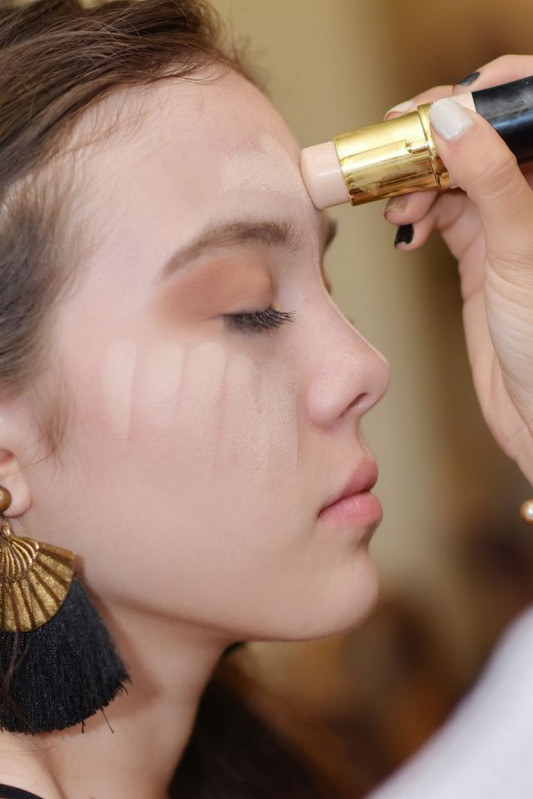 a woman applying a foundation stick layer on her face to get a non-cakey look. 