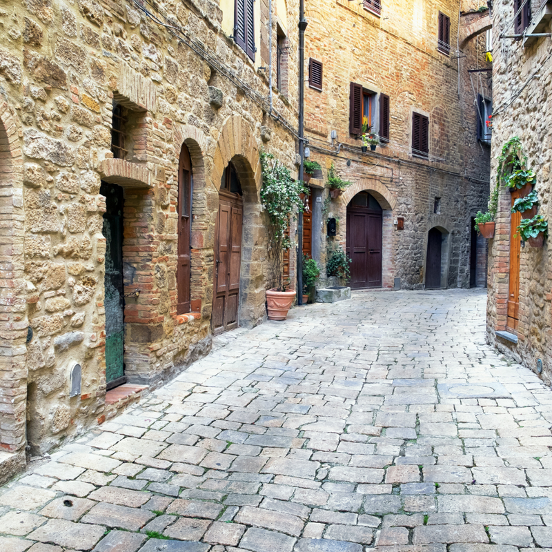 A cobblestone Italian alleyway lined with arched doorways