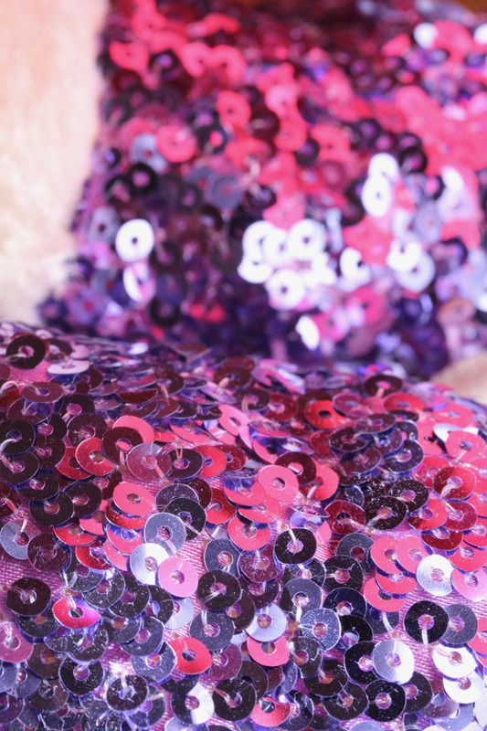 close-up of purple sequined fabric with something red reflected in the sequins