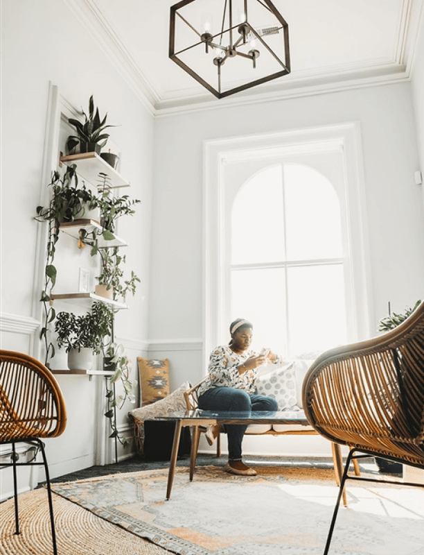 Bright and stylishly decorated lounge area with large windows and a person relaxing in a wicker chair.