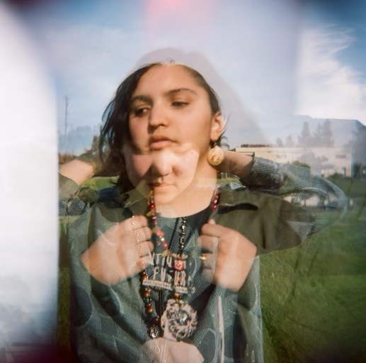 a photo that is double-exposure, layering one shot of my friend with lots of necklaces and a blue button up on as they look down over a photo of me holding a button up slightly open to show my necklaces and shirt as i look off to the side.