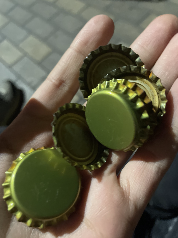 A photo of a hand holding eight bottle caps, each one a sort of dark silver tinted yellow-green. They're clean and plain.