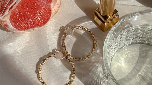 Hoop earrings placed on a table along with glass and a fruit