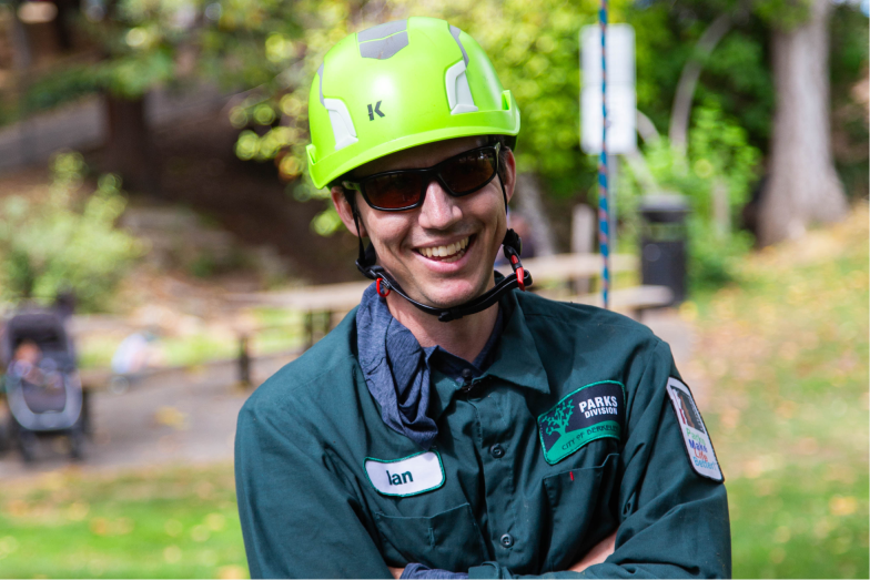 Ian is smiling and wearing his work uniform out in the park.