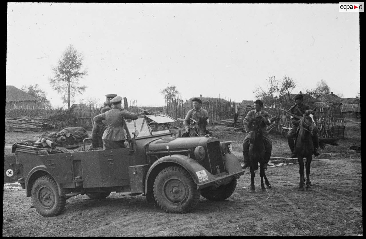 Des officiers allemands à bord d'un véhicule Horch Kfz.15 s'adressent à des hommes à cheval. Insigne