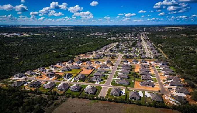 Aerial view of a Texas neighborhood showcasing houses, streets, and greenery under a clear blue sky.