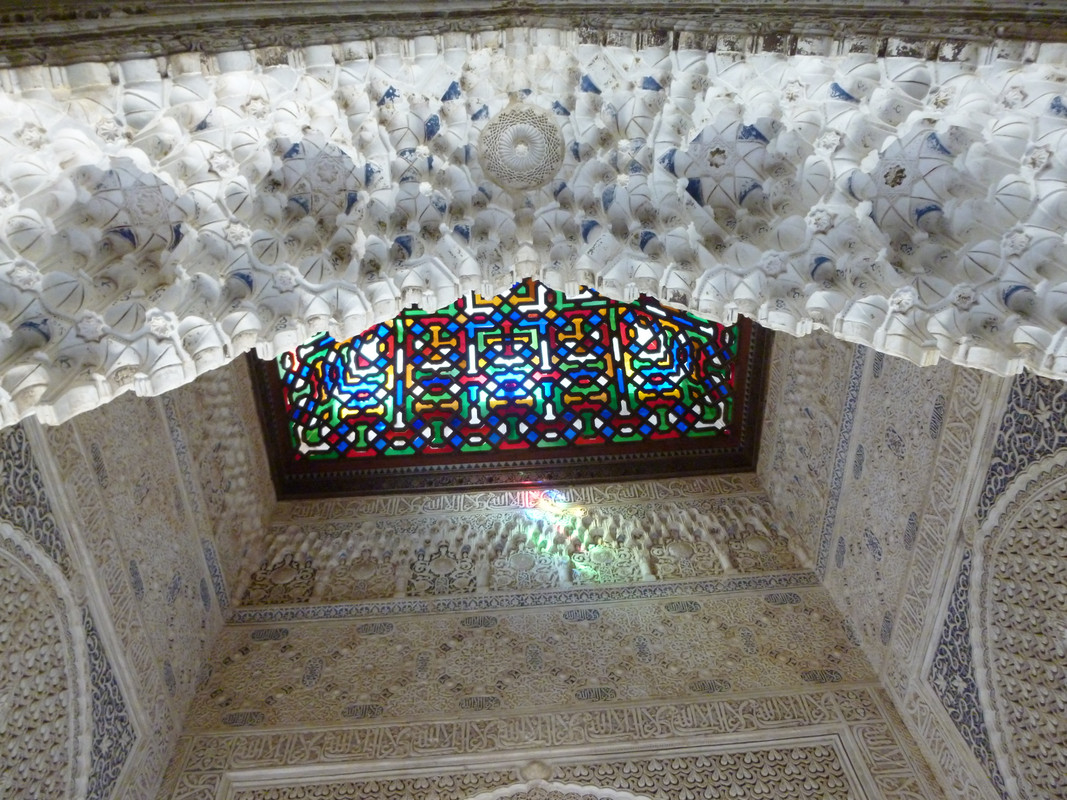 The muqarnas ceiling, which, as I said, looks like the most beautiful inverted termite mounds, takes up the top third of the picture.  They are white with blue highlights.  The centre of the next third is the stained glass, which is red, blue, green and yellow with the expected black lead lining.  The remainder of the photo is the white and blue detailed walls.