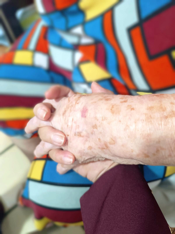 Mãos entrelaçadas, cuidadora e idoso em ILPI
