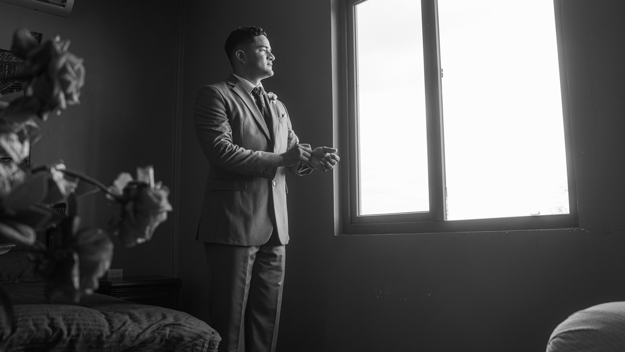 Previa del novio en blanco y negro viendo hacia la ventana
