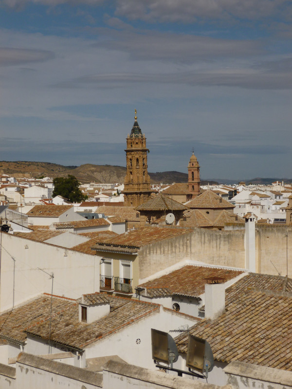 Photo over the top of more orange tiled houses.  In the centre is another church, the top of bell tower is in a black stone