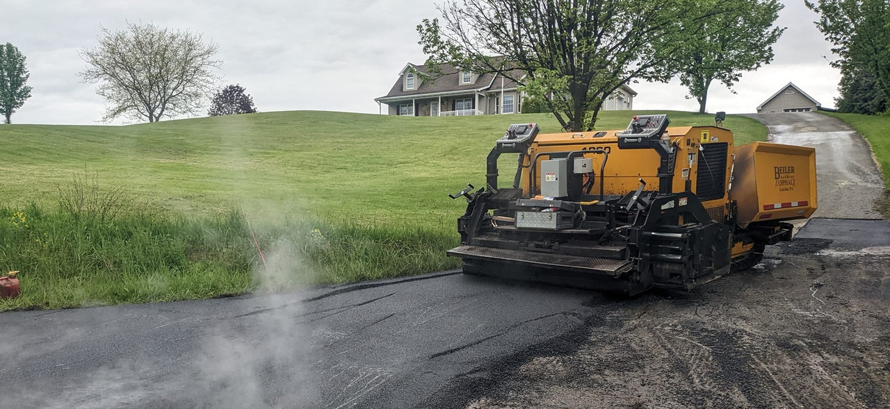 Asphalt paving machine laying fresh asphalt on residential driveway