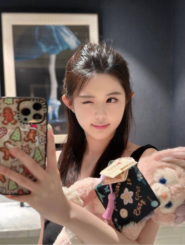 女子拿手機自拍並抱著粉色絨毛玩偶的室內生活感照片
