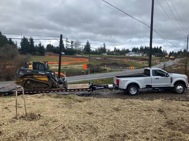 Compact track loader on a trailer behind a pickup at a jobsite