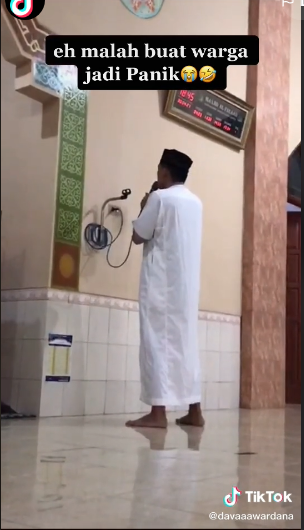 Seorang pemuda berbaju putih tengah mengumandangkan azan