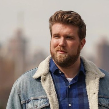 a stocky blonde man wearing a flannel shirt and denim jacket