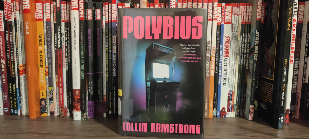 The Polybius book sitting on a book shelf in front of graphic novels.