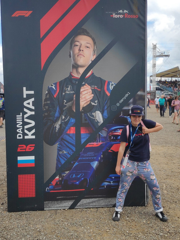 Hayley doing a JoJo pose in front of a Daniil Kvyat poster