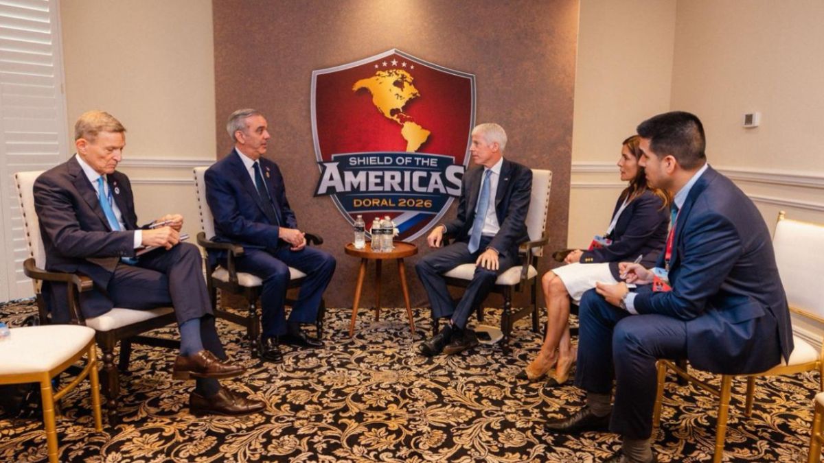 Luis Abinader y cuatro asistentes más sentados en una reunión formal ante el logo de Shield of the Americas 2026