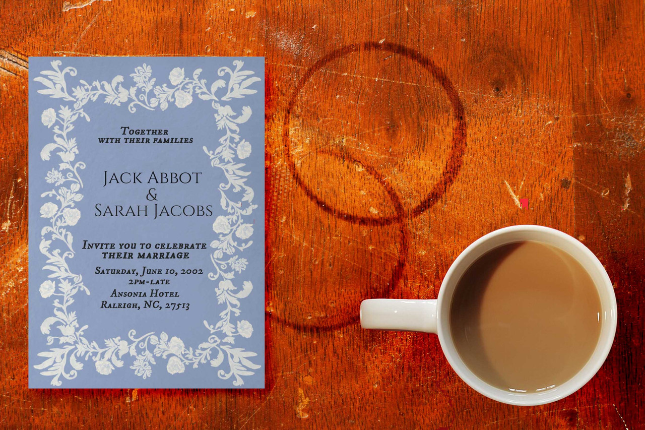 Photo from above of a table with a mug of tea on it. Next to it is Jack's wedding invitation