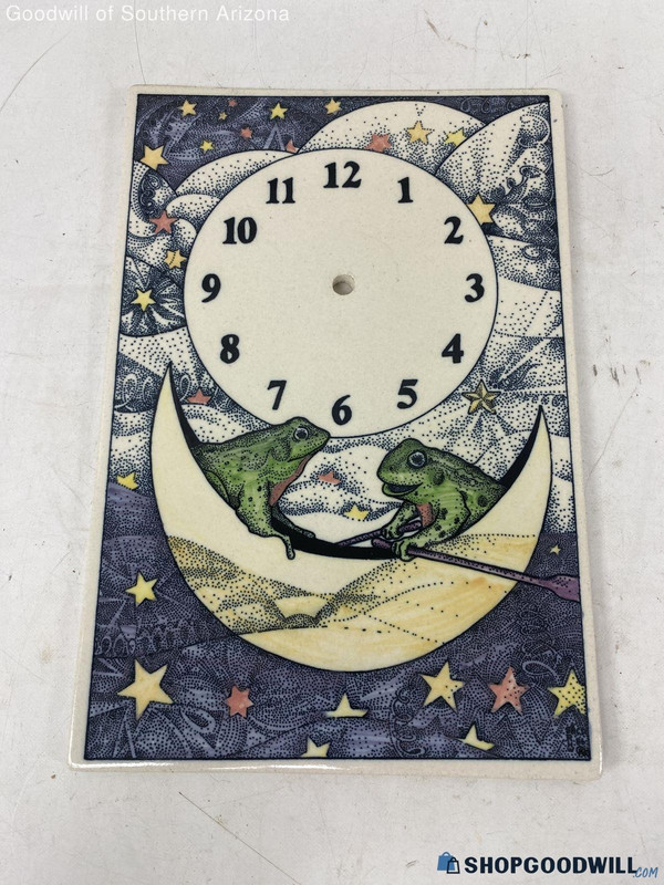 a product photo of a rectangular clock with no hands. under the clock face is an illustration of two green frogs in a crescent moon in an abstract starry sky. one of the frogs is holding oars as if the moon is their boat.