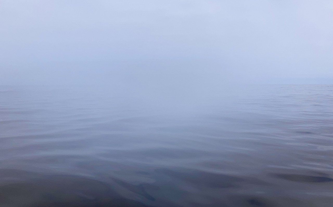 Picture of the ocean, calm dark waters fading into a pale grey sky with barely any visible horizon line