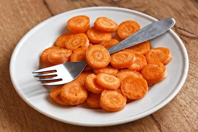 A plate containing chopped carrots with a fork in it