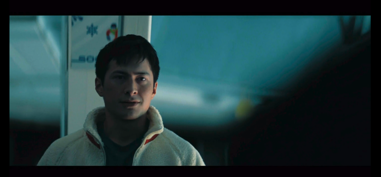 shane, framed from the chest up, fills the left side of the image. he's facing towards the camera and looking forward. the back of ilya's shoulder fills the right side of the image.