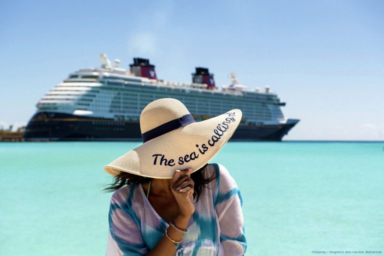 Mulher com chapéu na praia e um navio de cruzeiro ao fundo