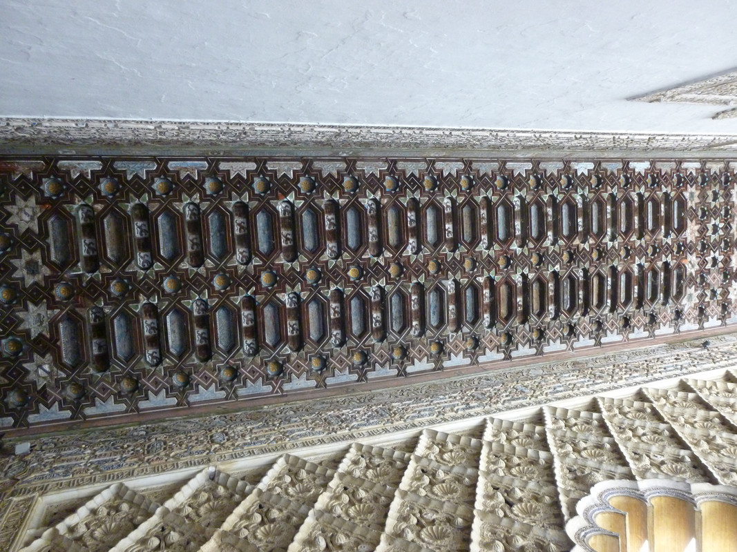 Ornately carved dark wood ceiling.  The shapes are repeating squares, lozenges, squares going down the photo and squares or lozenges in a row going horizontal along the photo.  At either end there are small star shapes.