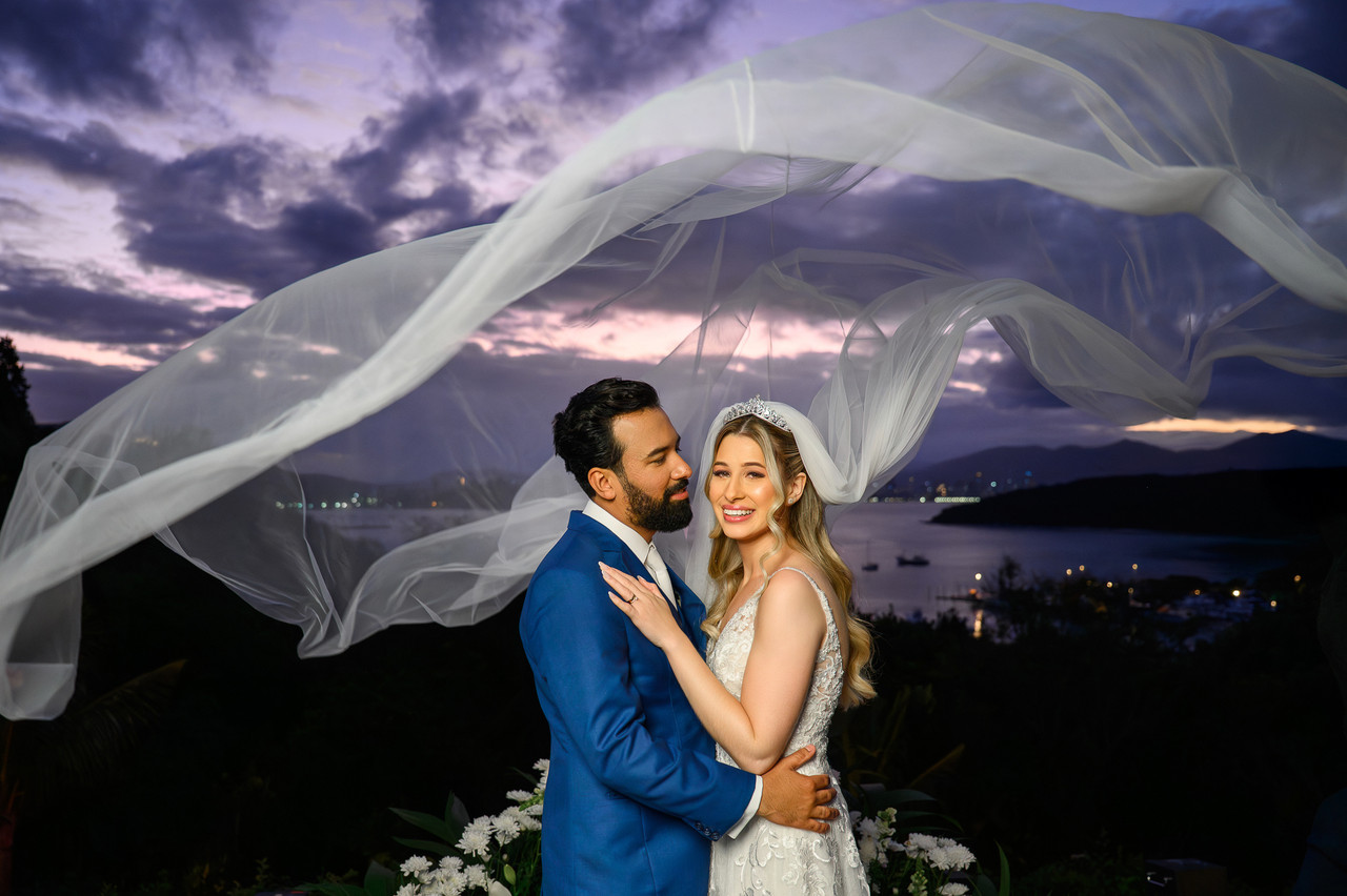 Noivos com véu ao vento e céu dramático no litoral de Santa Catarina