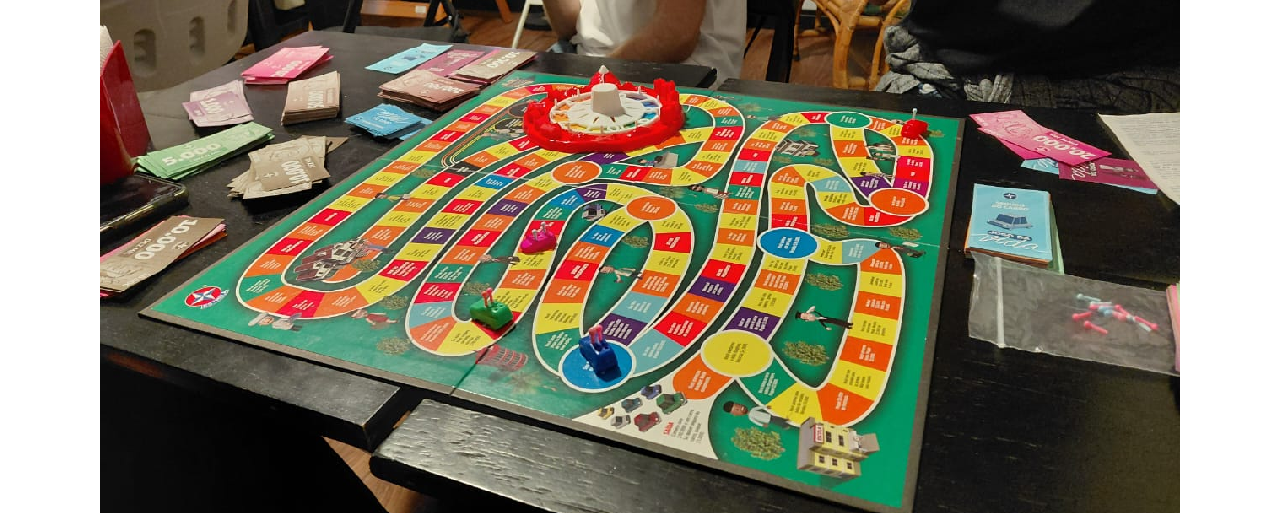Mesa de um bar com o tabuleiro do Jogo da Vida em cima