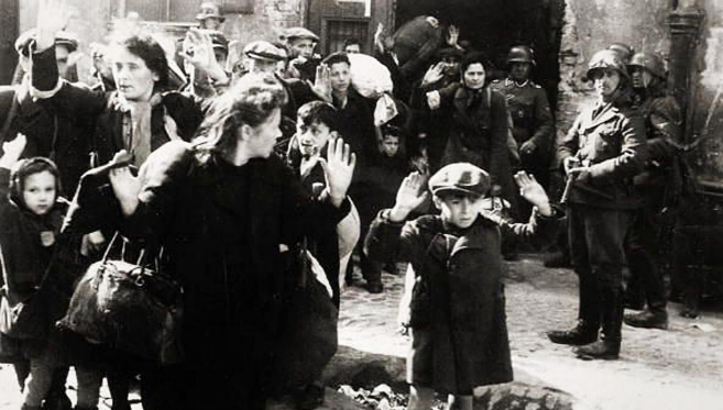 Varios judíos levantan la mano mientras un nazi les apunta con una pistola en el gueto de Varsovia, en 1943