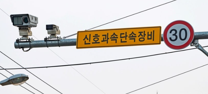 Korean fixed speed enforcement camera sign mounted on a traffic signal pole with a 30 km/h speed limit sign