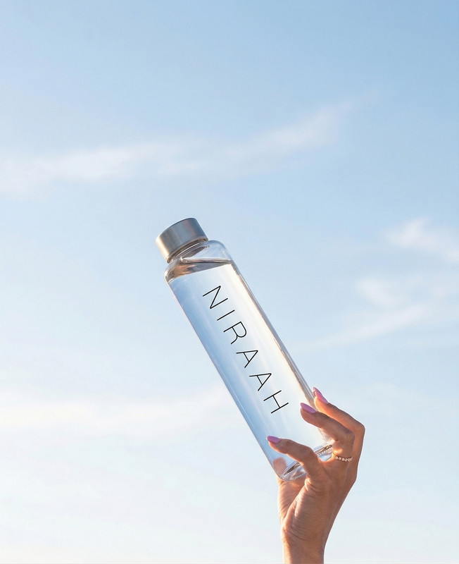 Niraah bottle styled against a minimal sky background