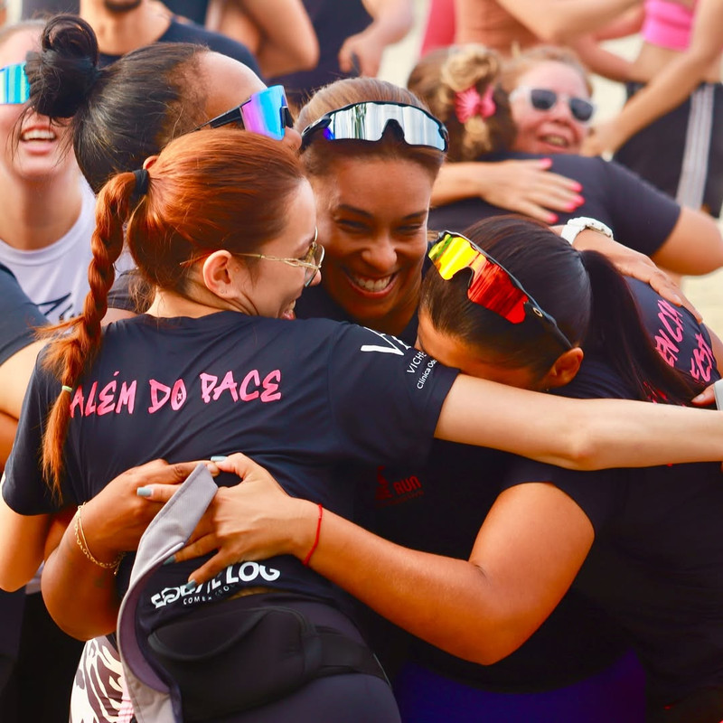 Grupo de corredoras sorrindo e se abraçando após um treino na praia.