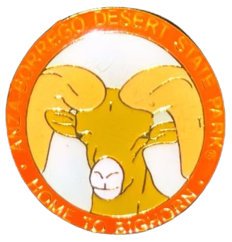 a glassy enamel pin with an orange ring around it that says 'ANZA-BORREGO DESERT STATE PARK * HOME TO THE BIGHORN' with a drawing of a bighorn sheep in warm colors in the middle
