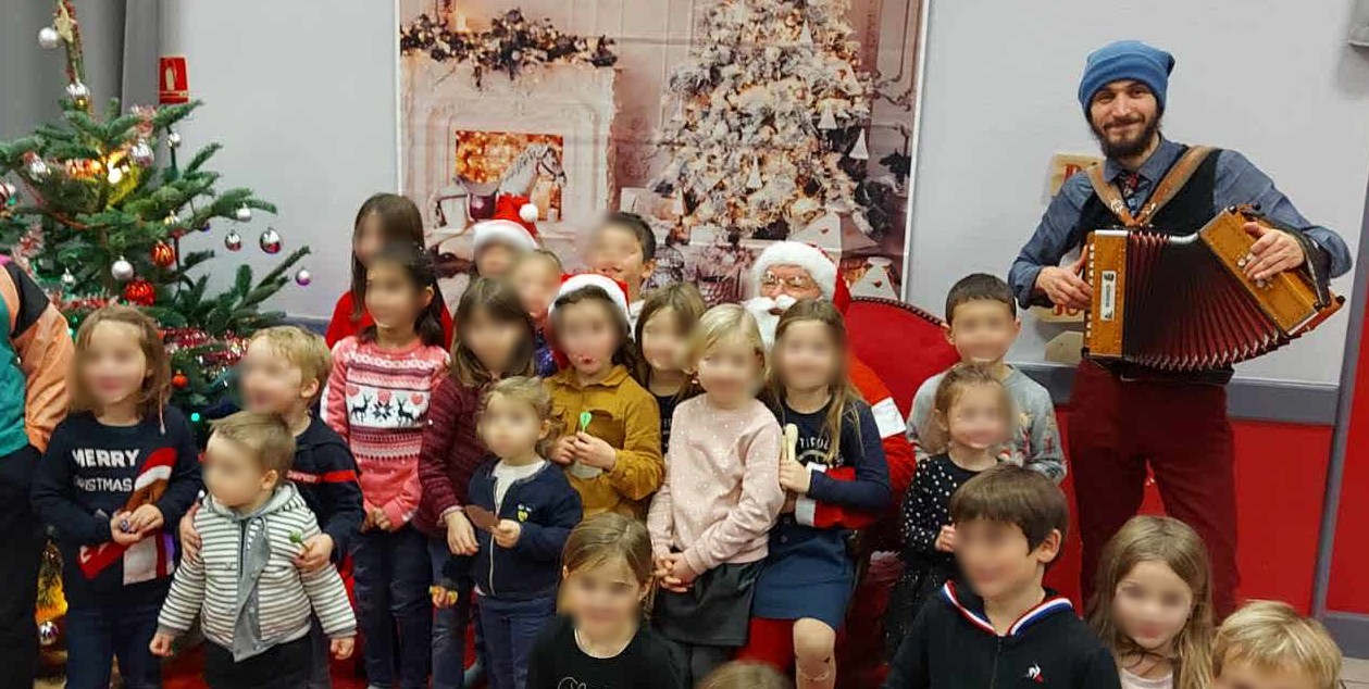 tout plein d'enfants très contents d'être pris en photos à côté du Père Noël qu'on distingue à peine derrière leurs petites têtes. et à droite, un accordéoniste ma foi très souriant.