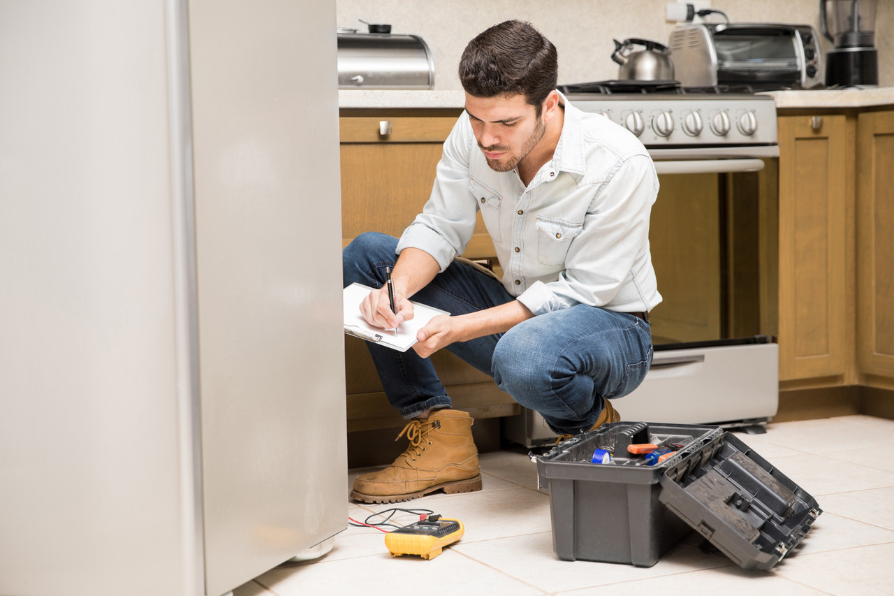 portrait handsome male technician doing work report broken fridge home kitchen