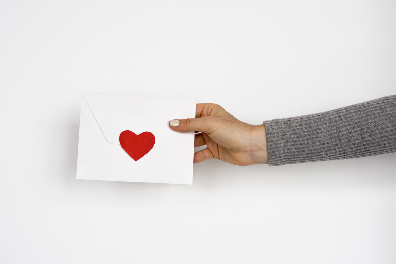Hand holding out envelope with a heart seal