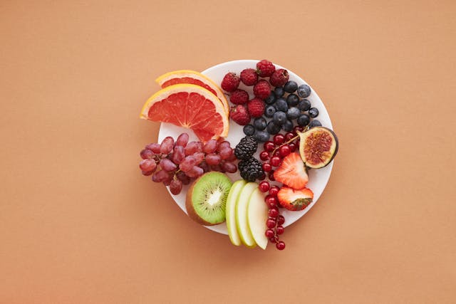 Plate of polyphenol-rich fruits, including berries, grapes, figs, kiwi, oranges, and apples, that promote gut microbiome health.