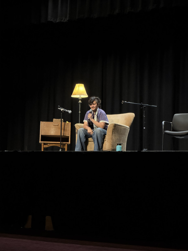 Photo of me on stage, sitting to read after introducing the event